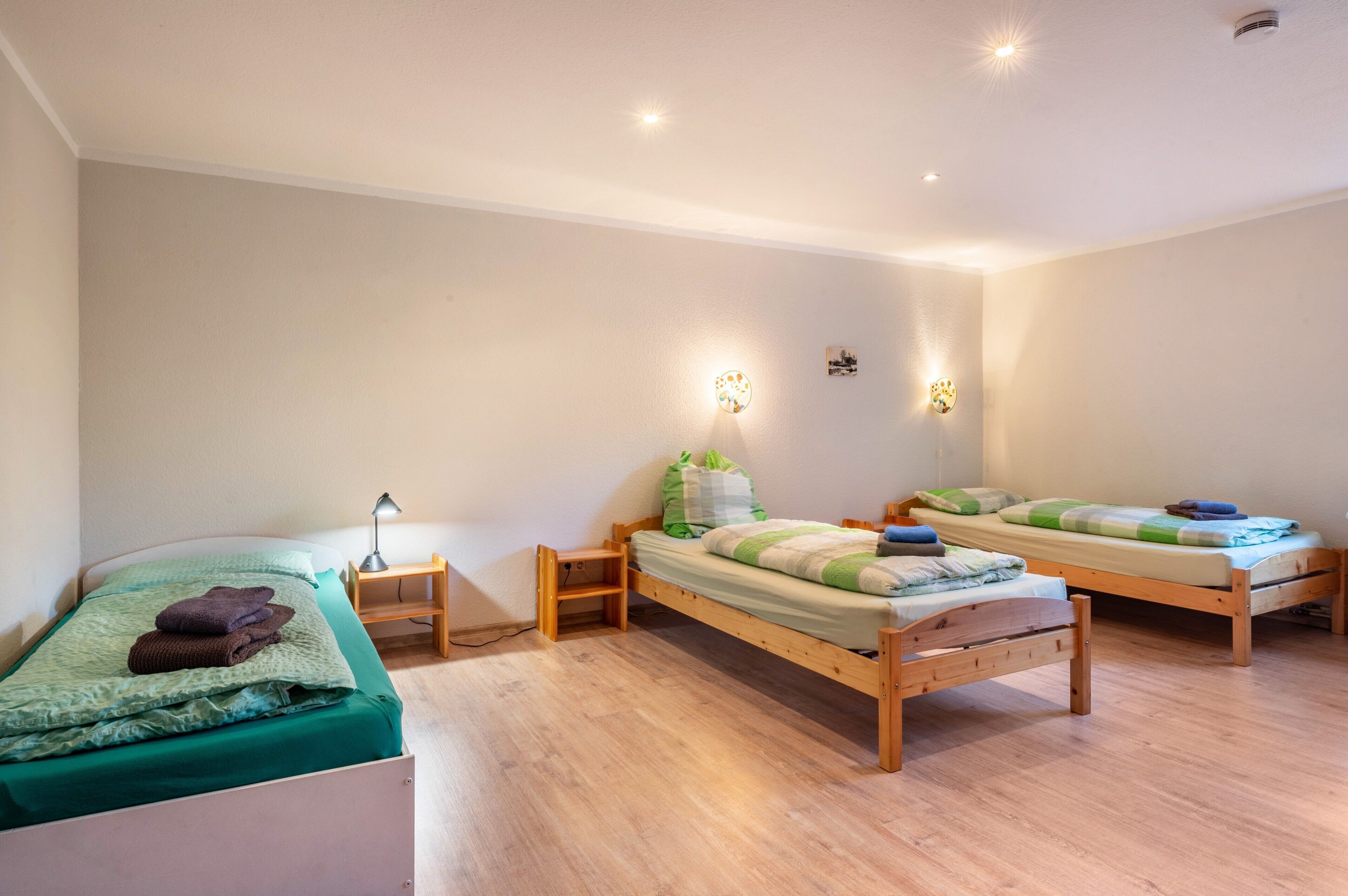 Een kamer met twee houten bedden, een klein nachtkastje van hout en een wandlamp.