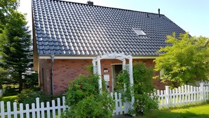 A brick house with a tiled roof, a white picket fence, and a small garden with a pathway leading to the entrance. - Apartment 'Ferienwohnung Abendsonne' with Wi-Fi (Lehe)