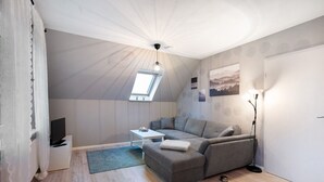 A modern living room with a sectional sofa, a flat-screen TV, a small table, a floor lamp, and a skylight. - Apartment 'Ferienwohnung Abendsonne' with Wi-Fi (Lehe)
