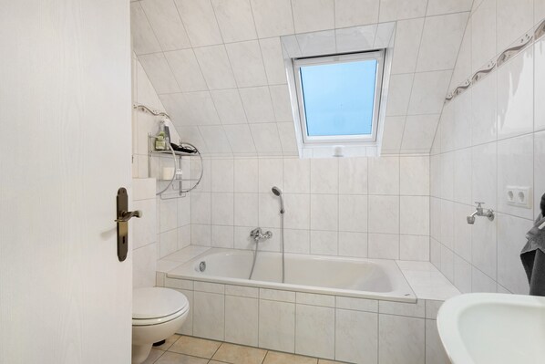 Une salle de bain avec une baignoire, des toilettes et une fenêtre située au-dessus de la baignoire.