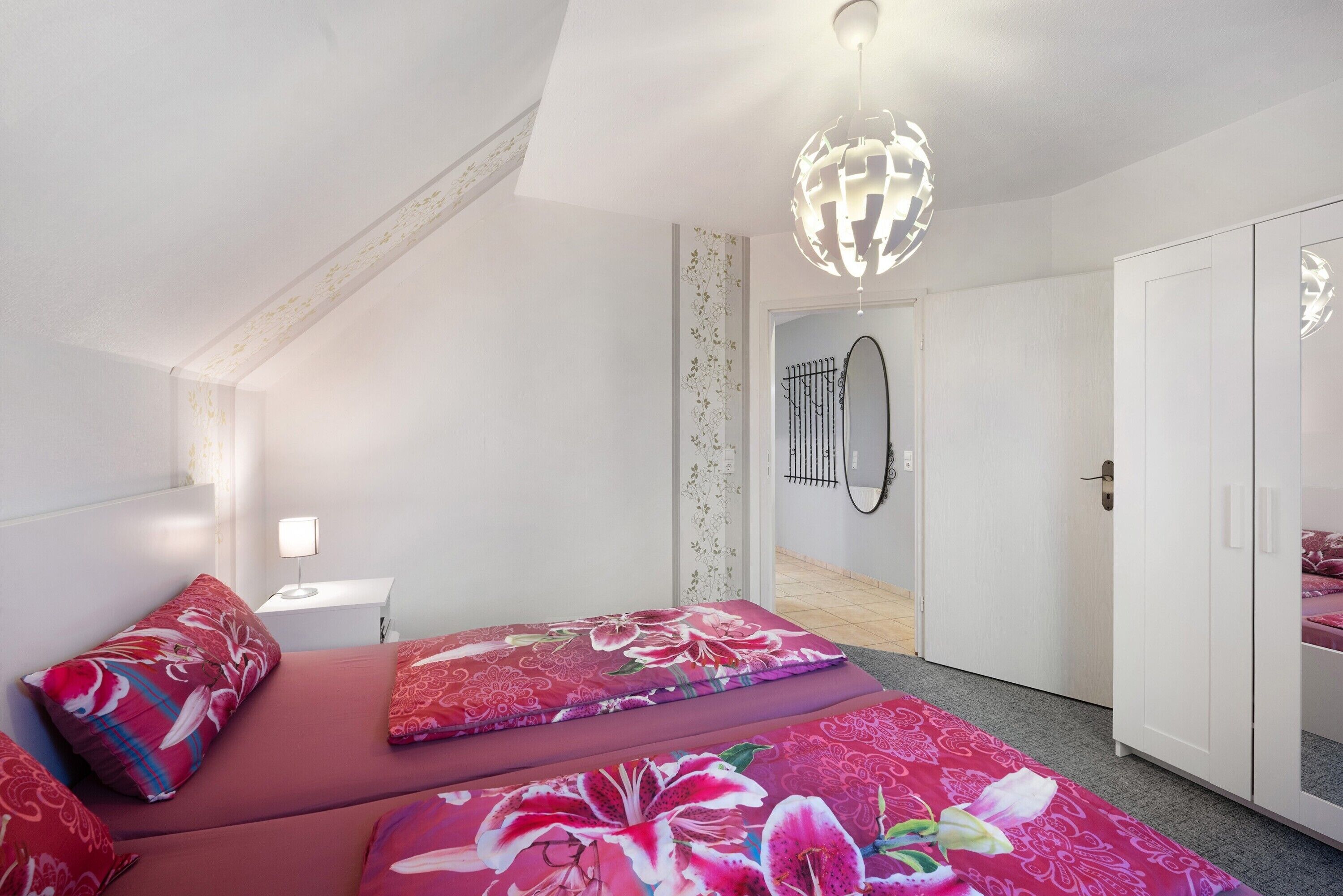 A bedroom with a bed, a nightstand, a wardrobe, and a door leading to another room.