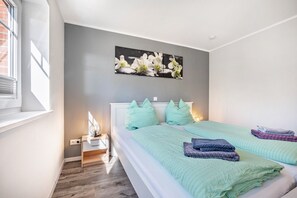 A bedroom with a bed, pillows, a nightstand, a wall-mounted picture, and a window.