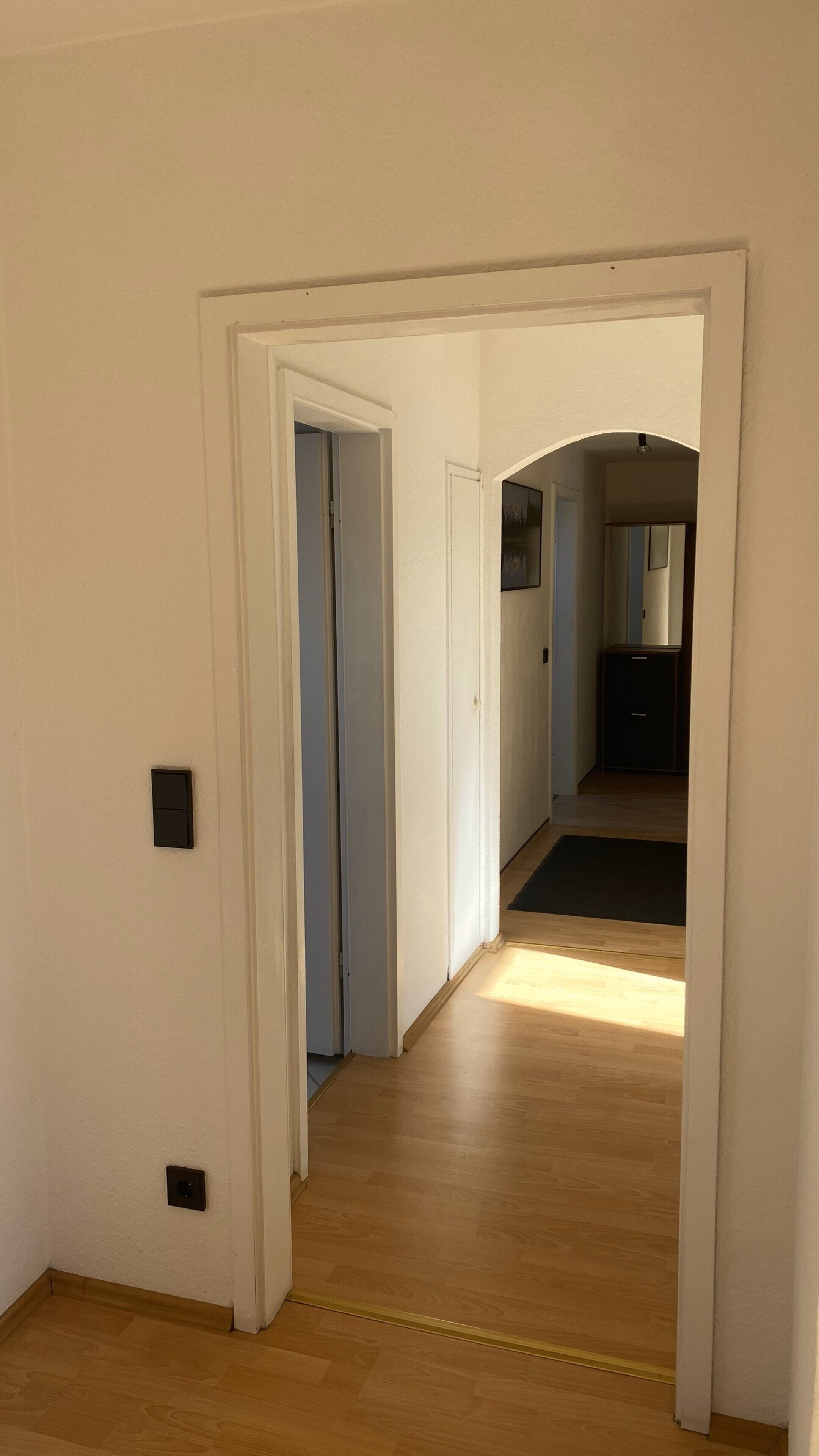 Ein Korridor mit Holzboden, weißen Wänden und einer Tür zu einem anderen Raum.
