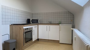 Cocina compacta con microondas, horno y armarios blancos.