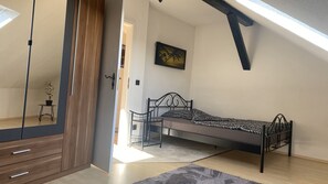 Un dormitorio con una cama, una mesita de noche, una silla, una pequeña mesa con una planta, un cuadro en la pared y un tragaluz.