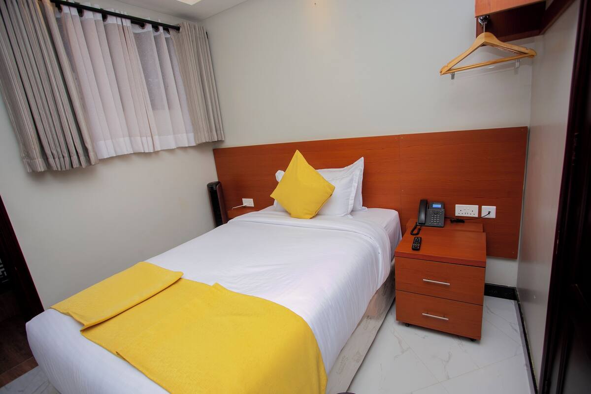 A hotel room with a bed, a wooden headboard, a bedside table with a phone, and a small drawer unit.