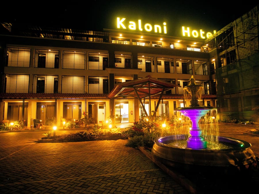 Ein Hotel namens 'Kaloni Hotel' mit einer hell beleuchteten Beschilderung, einem Springbrunnen und einem gepflasterten Eingangsbereich.