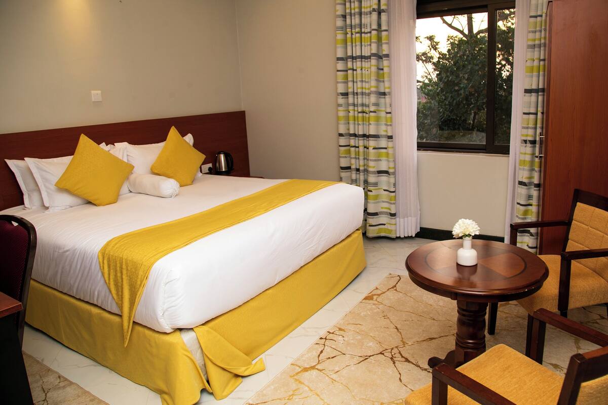 A hotel room with a bed, a round wooden table, and two chairs.