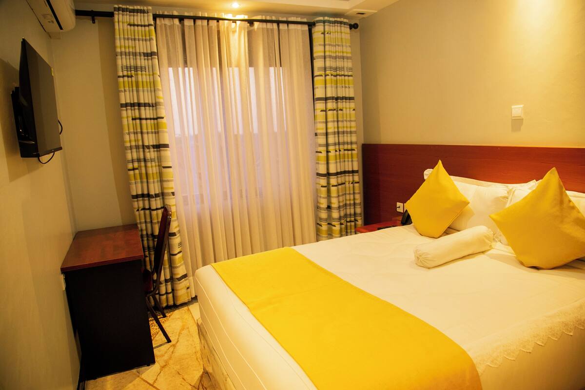 A hotel room with a bed, curtains, a TV, and a small table.