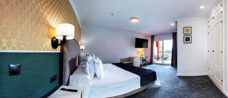 A hotel room with a curved bed, a desk, a chair, a TV, and a balcony with a view.