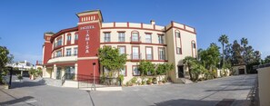 A multi-story hotel with a prominent red and beige facade, multiple balconies, and a well-maintained outdoor area with potted plants. - Hotel Tamisa (Mijas)