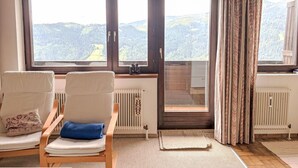 A room with two white chairs, a view of a mountainous landscape through large windows, and a radiator. - Daniele by Interhome (Mühlbach am Hochkönig)