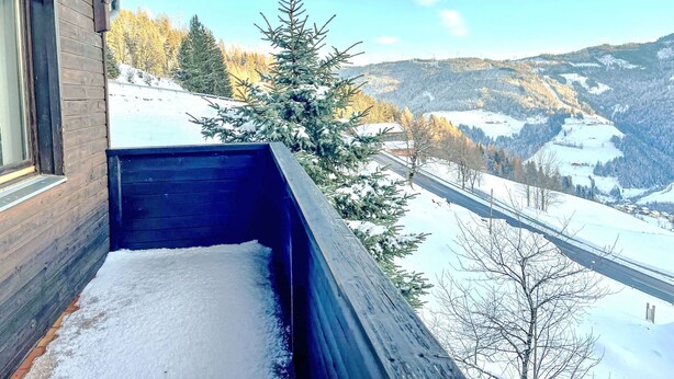 A wooden balcony with a snow-covered ledge and a view of a snowy landscape with trees and hills. - Daniele by Interhome (Mühlbach am Hochkönig)