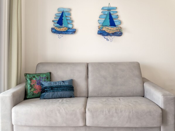 A grey sofa with two decorative pillows and a wall-mounted sailboat decoration. - La terrazza sulla piscina by Interhome (Valledoria)