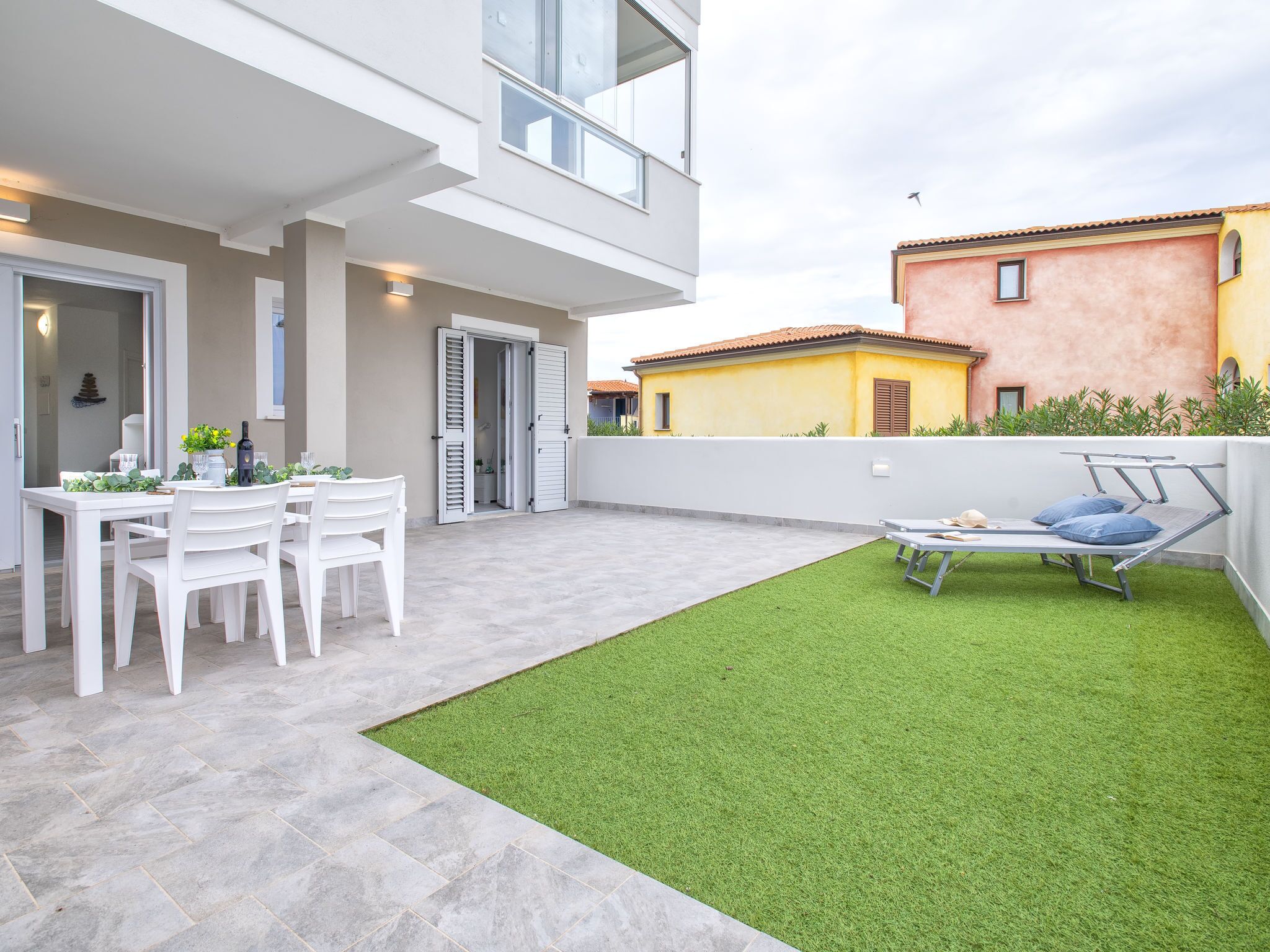 A modern outdoor patio with a dining table and chairs, a small grassy area, and a bed.