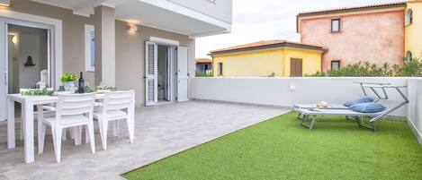 A modern outdoor patio with a dining table and chairs, a small grassy area, and a bed.