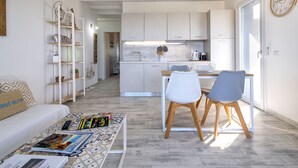 A modern, open-plan living and dining area with a sofa, coffee table, and chairs. A kitchen with white cabinets and a dining table is visible in the background. - Mare Azzurro by Interhome (Valledoria)