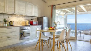 A modern kitchen with white cabinets, a wooden floor, and a dining area with white chairs. - Onda perfetta by Interhome (Valledoria)