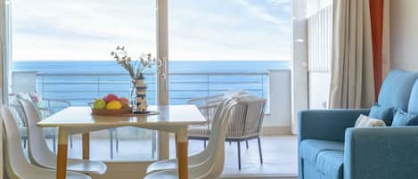 Un balcón con vista al océano, una mesa de comedor con sillas y un sofá azul.