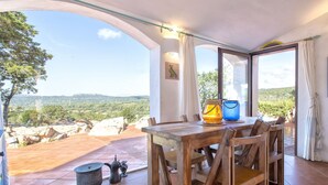 Un comedor con mesa y sillas de madera, vista al campo y un ventanal con cortinas.