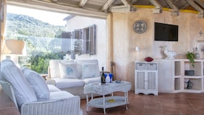Un rincón al aire libre acogedor con mobiliario de mimbre, una pequeña mesa con una botella y vasos, y un aparador decorativo.
