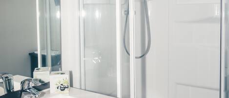 A modern bathroom with a white sink, a mirror, and a glass-enclosed shower.