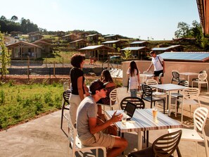 Un espace extérieur aménagé avec des tables et des chaises, entouré d’une clôture et de verdure.