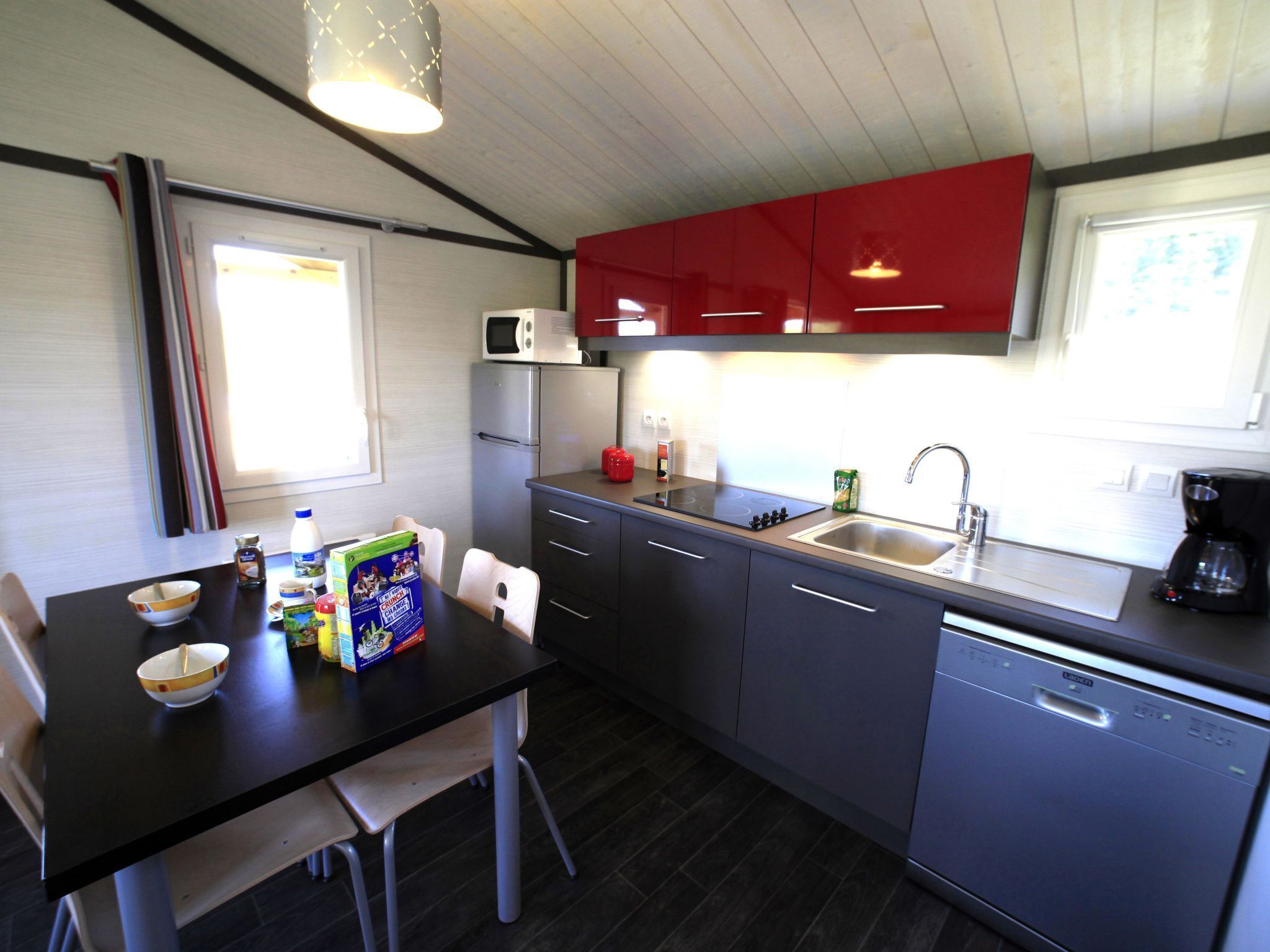 Eine kleine Küche mit Kühlschrank, Mikrowelle und Spüle. Ein Esstisch mit Stühlen und einigen Gegenständen steht daneben.