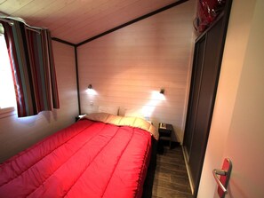 Une chambre à coucher avec un lit rouge, des murs en bois, deux lampes de chevet, une table de chevet et une porte avec une poignée.
