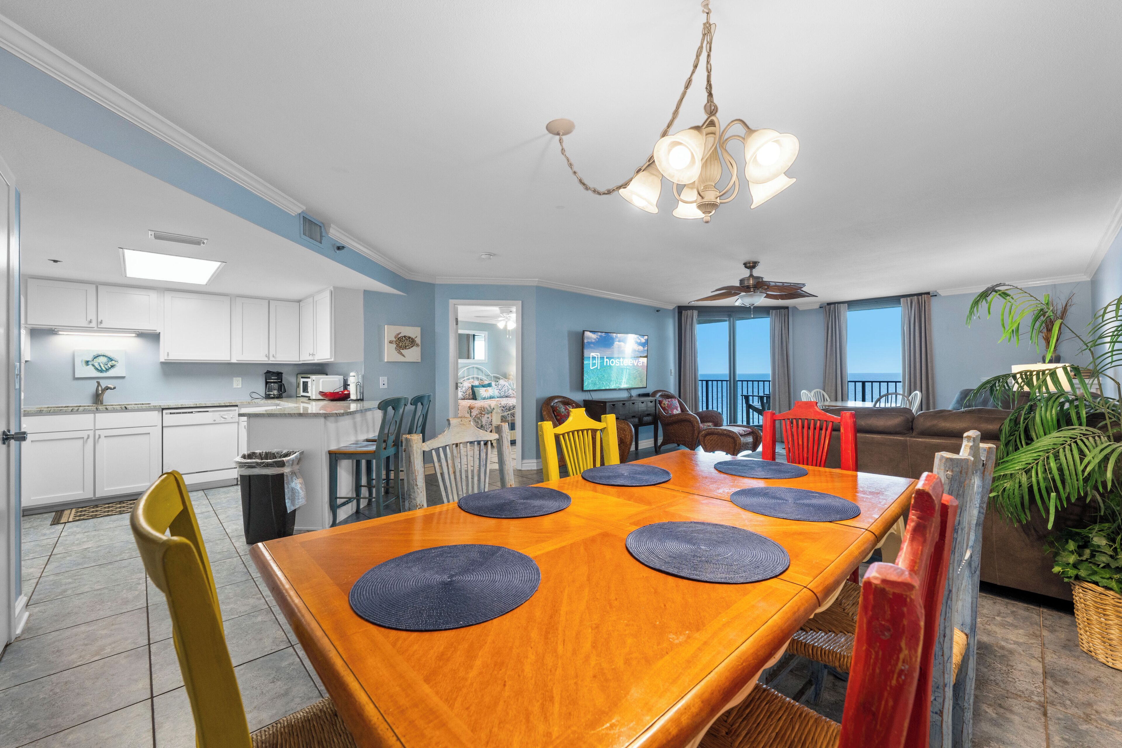 A spacious dining area with a wooden table and chairs, a kitchen with white cabinets, and a living area with a sofa and a television.
