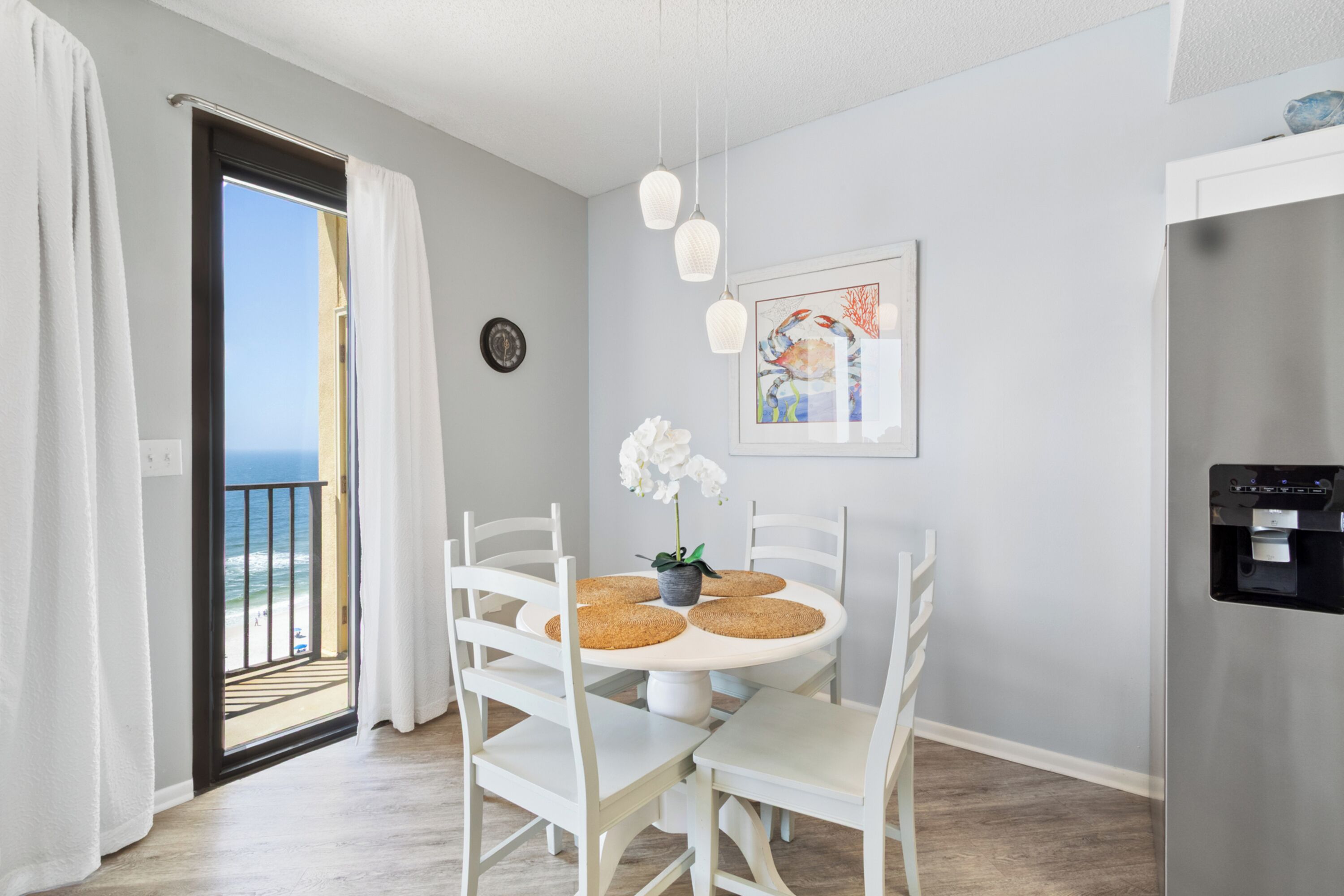 A dining area with white chairs, a round table, and a view of the ocean through an open door.