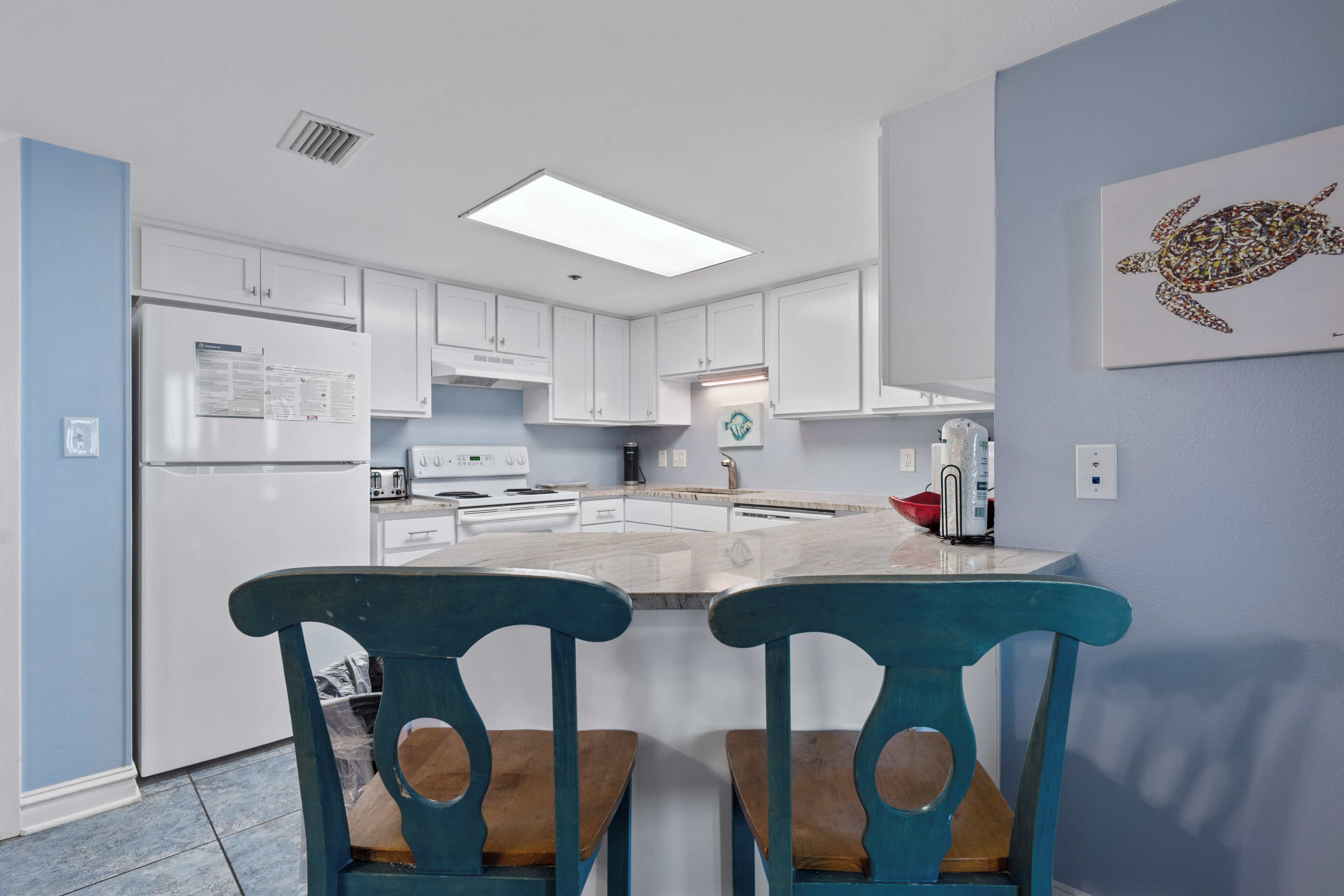 A modern kitchen with white cabinets, a central island, and two blue chairs.