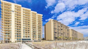 A high-rise hotel with multiple balconies, a beach view, and a sandy walkway. - Phoenix IV Condos (Orange Beach)