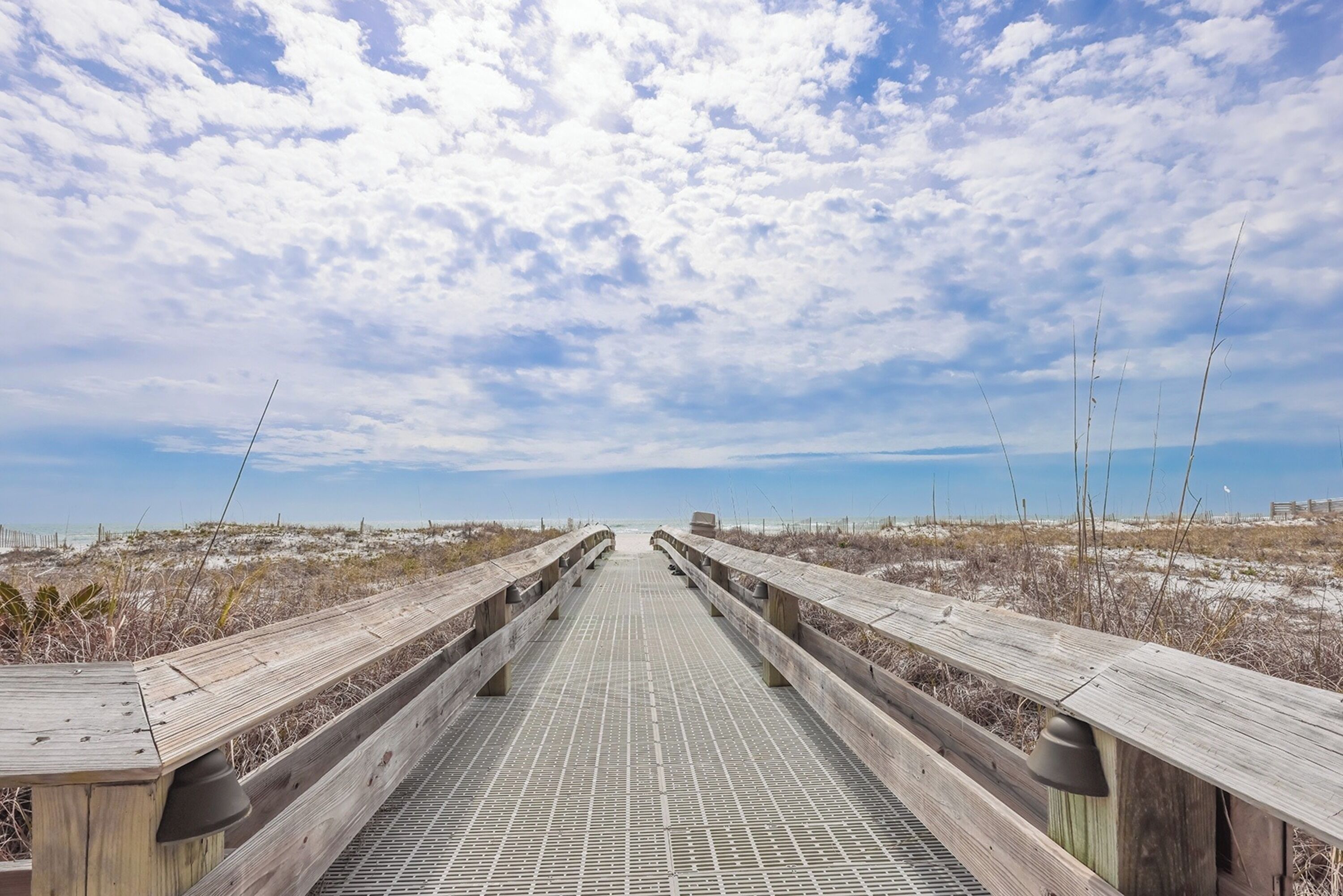 A wooden boardwalk leading to a beach with a clear sky.