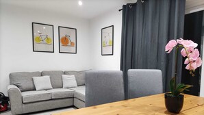A modern living room with a grey sofa, two framed pictures on the wall, a wooden table with a potted orchid, and grey chairs.