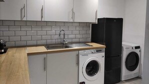 A compact kitchen with white cabinets, a stainless steel sink, a black refrigerator, and a front-loading washing machine.