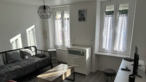 A modern living room with a sofa, a red chair, a wooden coffee table, a white desk with a computer, and a radiator. - Full center  (Le Malesherbois)