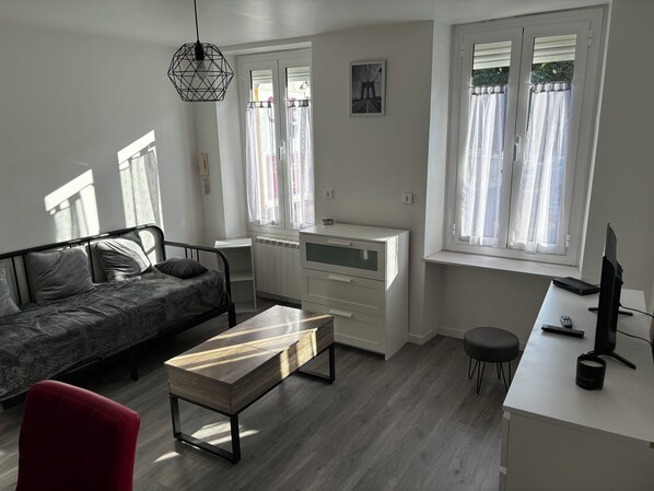 A modern living room with a sofa, a red chair, a wooden coffee table, a white desk with a computer, and a radiator.