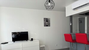 A modern living room with a flat-screen TV, white cabinetry, a small stool, and red bar stools. - Full center  (Le Malesherbois)