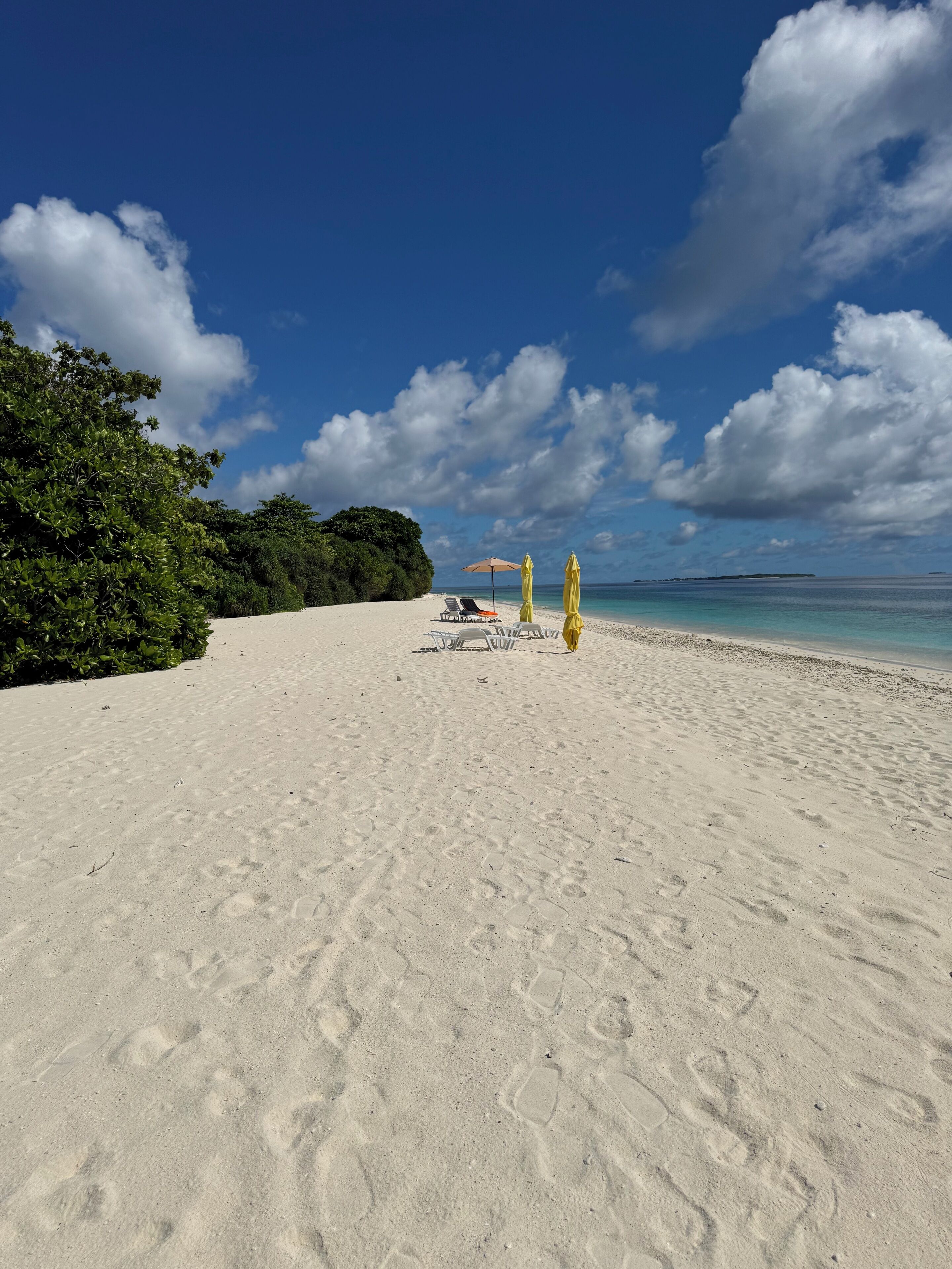 A beach with white sand, a few umbrellas, and lounge chairs.