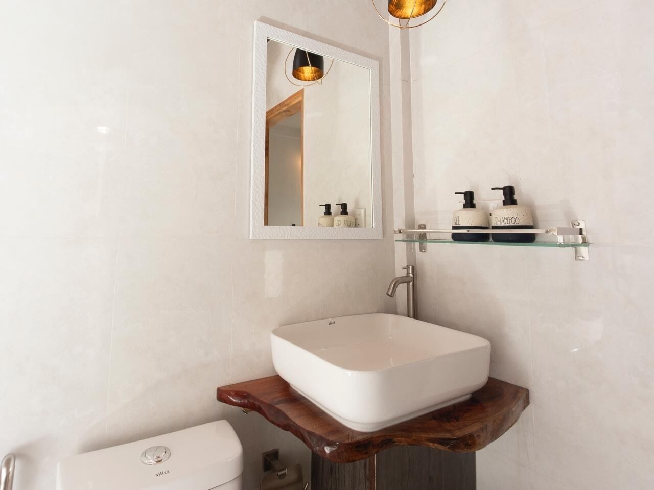Une salle de bain avec un lavabo blanc, un miroir, des toilettes et une étagère contenant des articles de toilette.