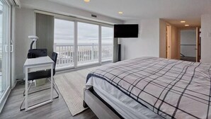 Ein Hotelzimmer mit einem großen Bett, einem Schreibtisch, einem Sessel, einem Fernseher und einem Balkon mit Blick.