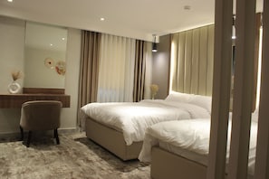 A modern bedroom with a large bed, a bedside table, a chair, and a mirror. - Azmal Hotel & Suites (Irbid)