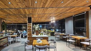 A modern restaurant with wooden ceiling and walls, multiple seating areas, and large windows. - Azmal Hotel & Suites (Irbid)