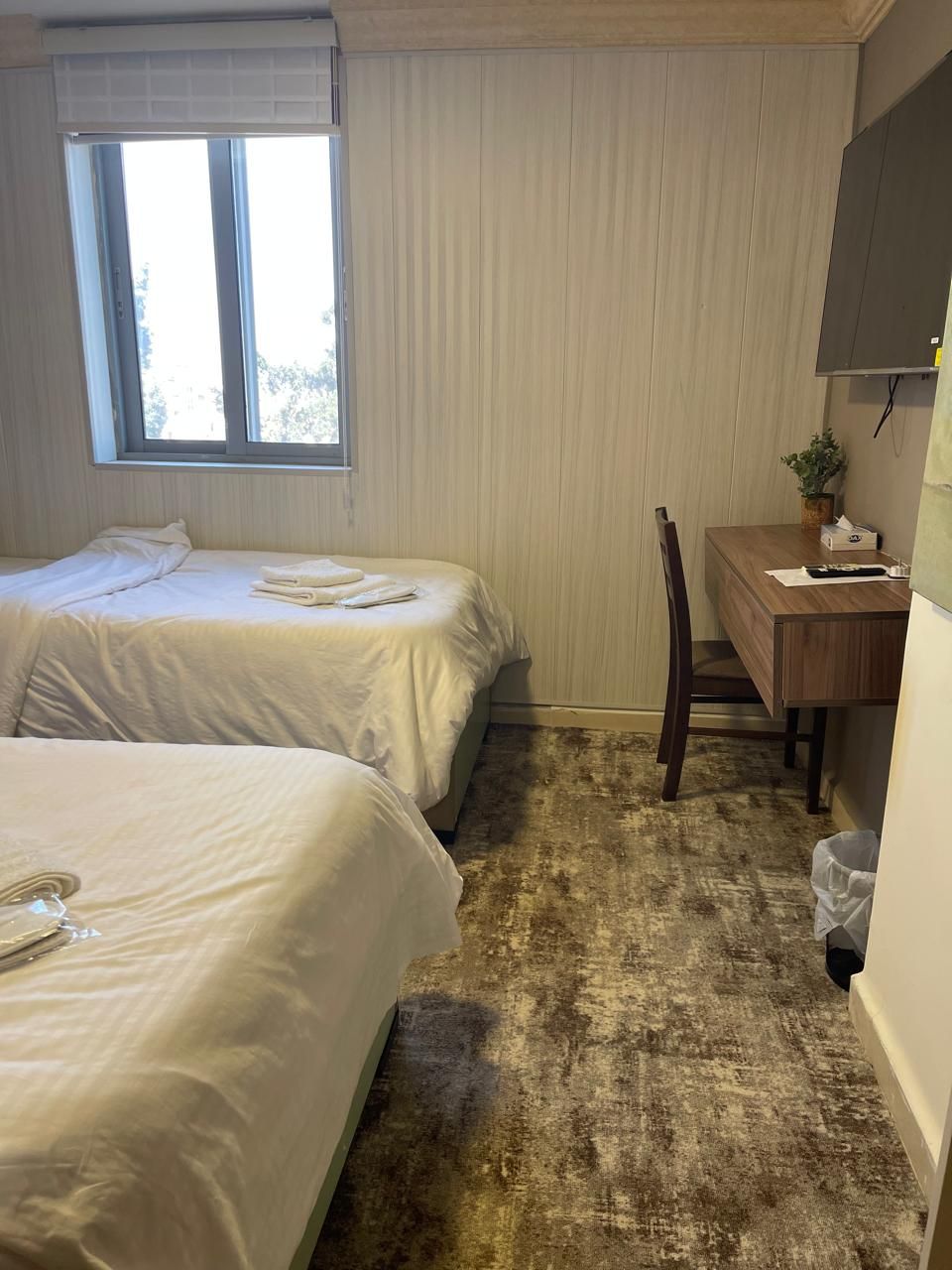 A hotel room with two beds, a desk, a chair, a window, and a curtain.