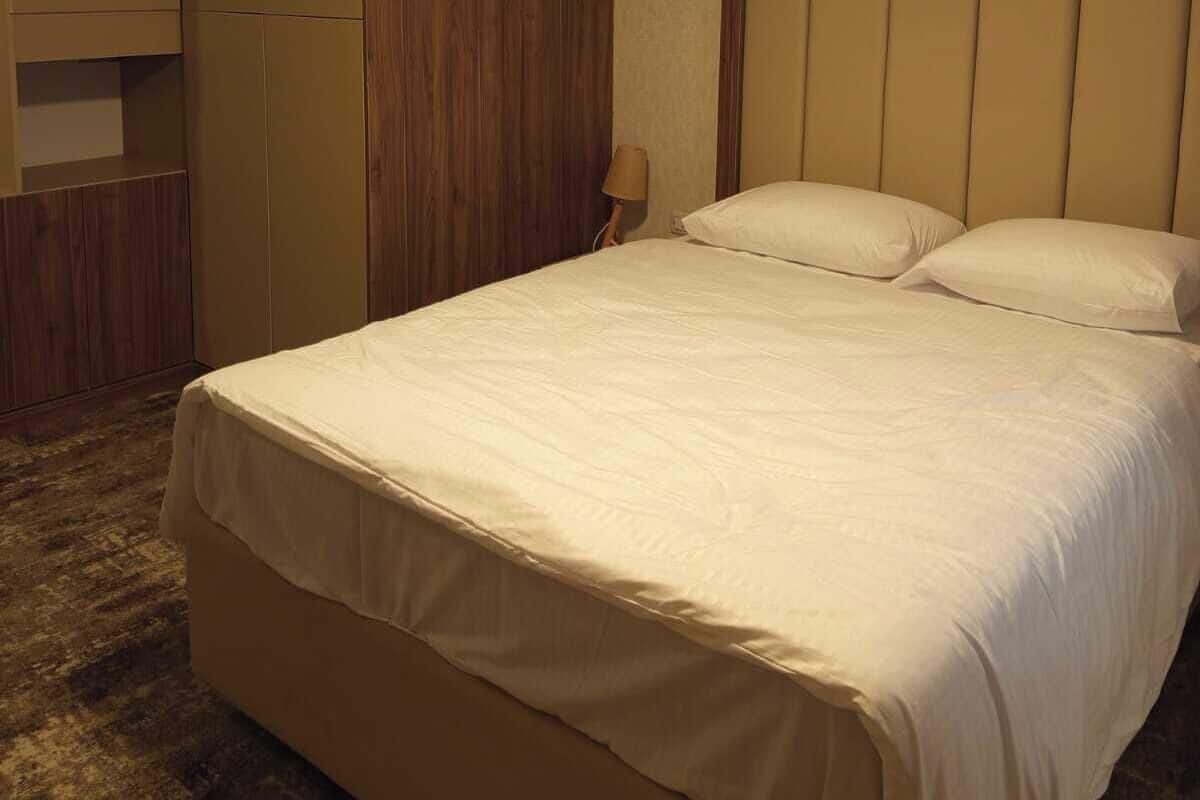 Hotellihuone, jossa on sänky, vaatekaappi ja kattoon asennettu ilmastointilaite.