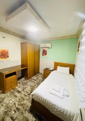 A bedroom with a bed, a desk, a wardrobe, and a nightstand. - Azmal Hotel & Suites (Irbid)