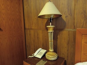 A wooden-paneled wall with a vintage-style lamp and a white rotary phone on a wooden nightstand. - Azmal Hotel & Suites (Irbid)