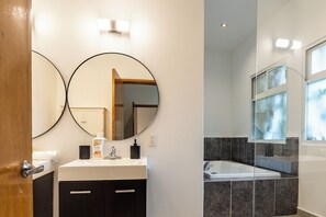Un baño moderno con un lavamanos blanco, dos espejos redondos, un mueble negro, una cabina de ducha con paredes de vidrio y una ventana con vistas.