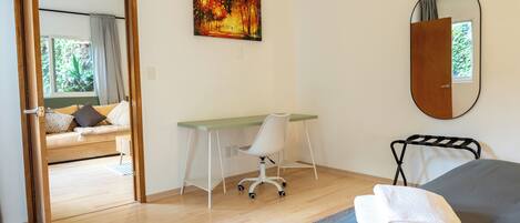A bedroom with a bed, a desk, a chair, a mirror, and a painting on the wall.
